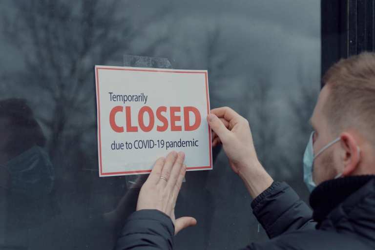 man hanging closed COVID-19 sign